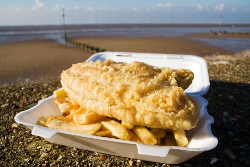 Een bakje met Engelse Fish and chips met op de achtergrond de zee 